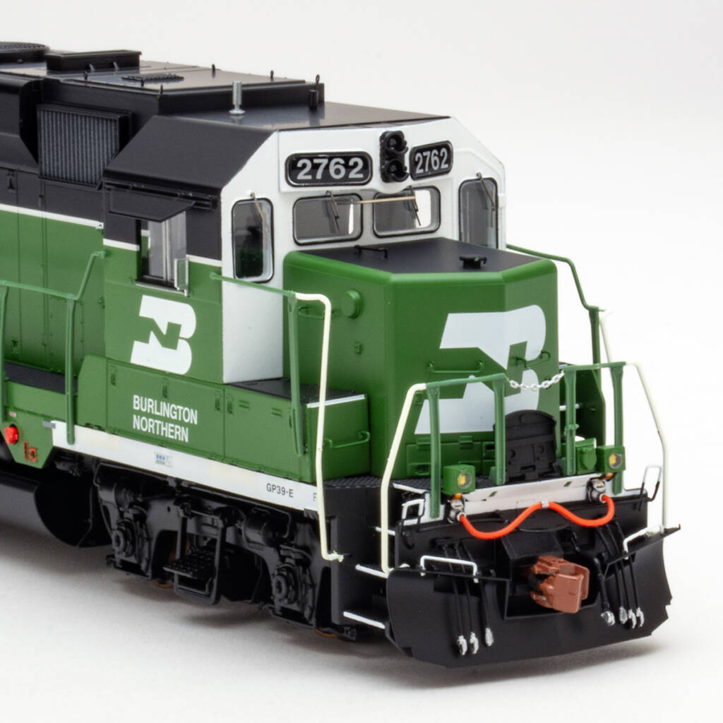 Color photo showing cab and short hood of HO scale diesel painted green, white, and black on white background.