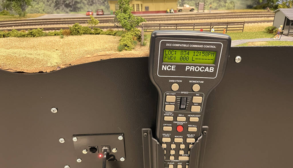 A DCC controller is mounted to the front of a model railroad layout
