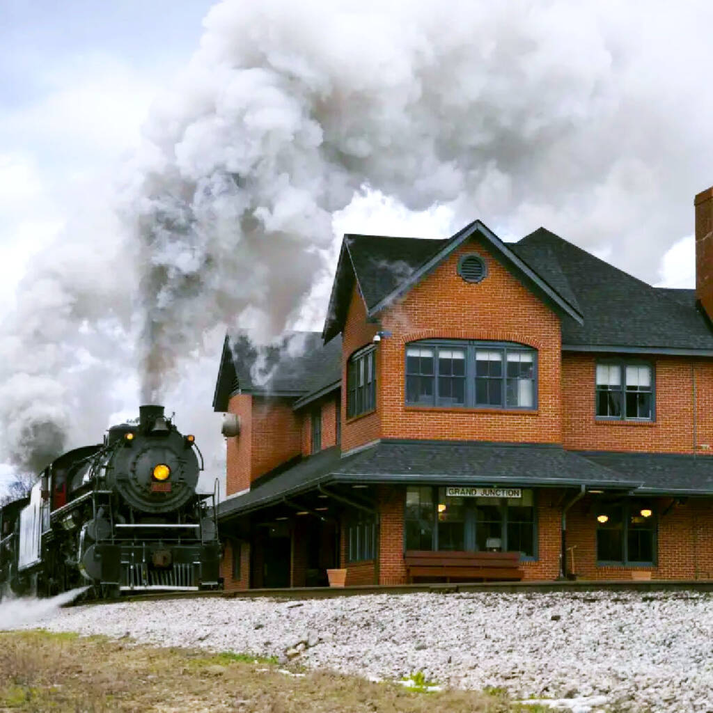 Black steam locomotive arriving next to a red brick depot building. Tennessee Valley Railroad Museum awarded $100K improvement grant.