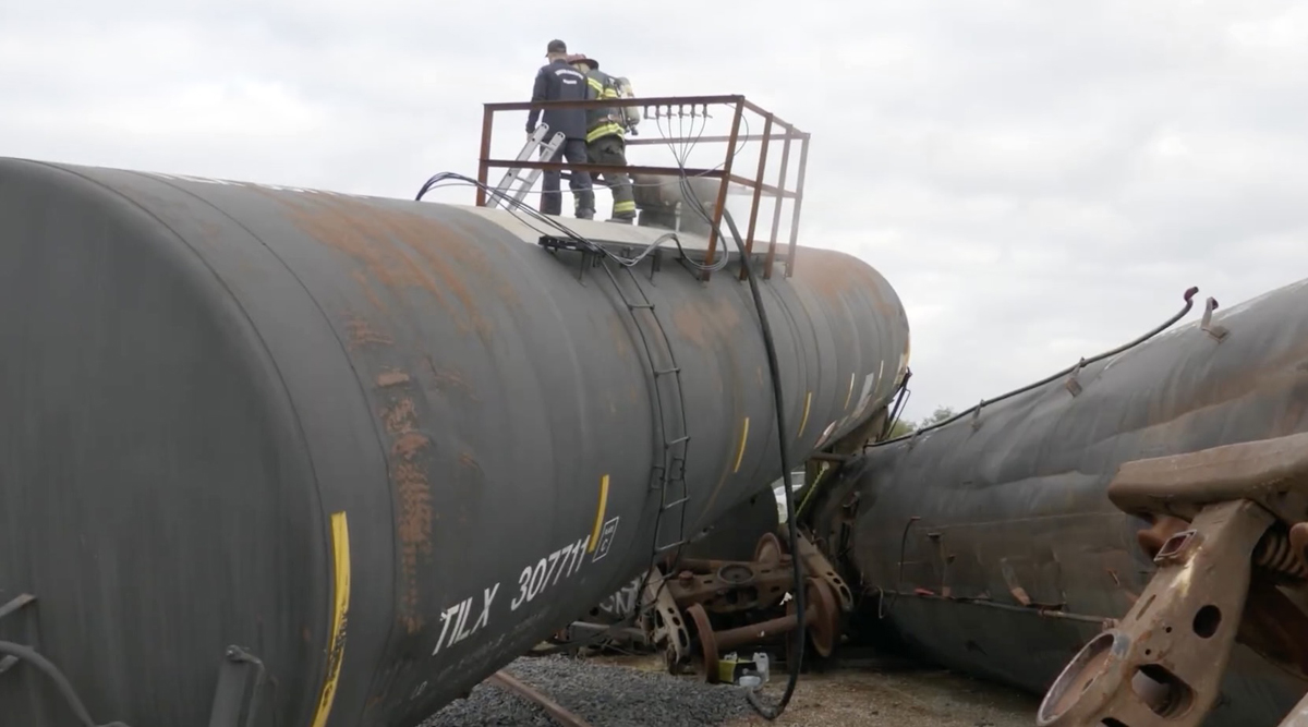 Two firefighters standing on top of tank car stacked to simulate derailment