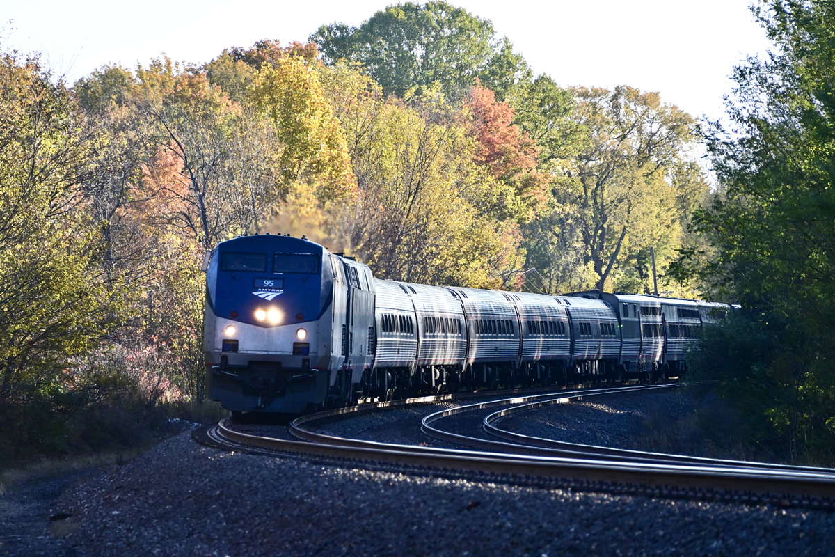 Passenger train rounding curve with background of trees displaying fall colors