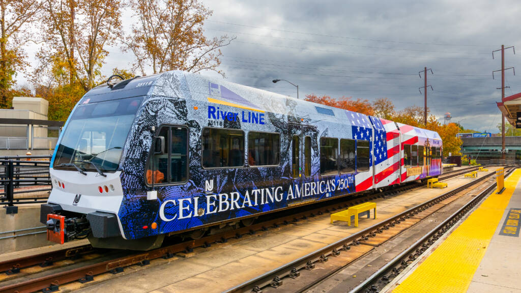 Light rail vehicle wrapped with design including U.S. flag, Revolutionary War imagery, and the words "Celebrating America's 250th"