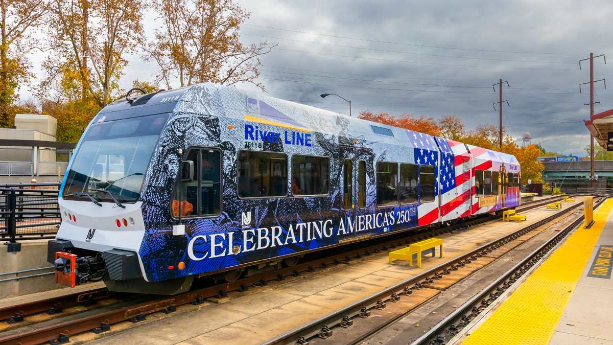 Light rail vehicle wrapped with design including U.S. flag, Revolutionary War imagery, and the words "Celebrating America's 250th"