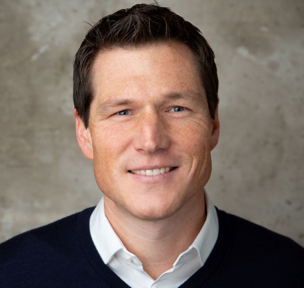 Smiling dark-haired man in black sweater and white shirt