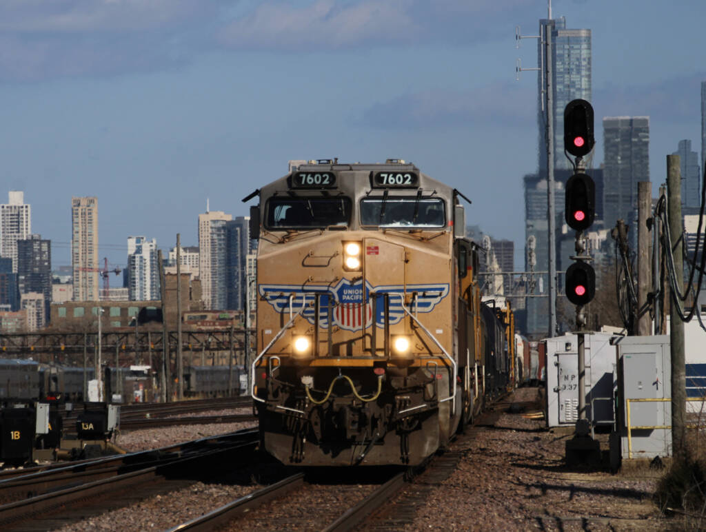 Freight train led yellow locomotive with Chicago skyline in background