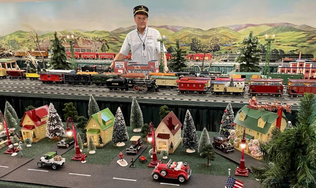 man standing next to holiday train layout