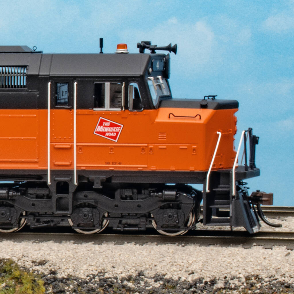Color photo showing engineer's side of cab on HO scale diesel with cowl body painted orange and black on scenicked base with a sky blue background.