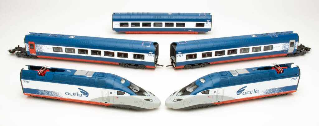 Color photo showing two modern streamlined locomotives and three passenger cars in red, white, and blue paint on white background.