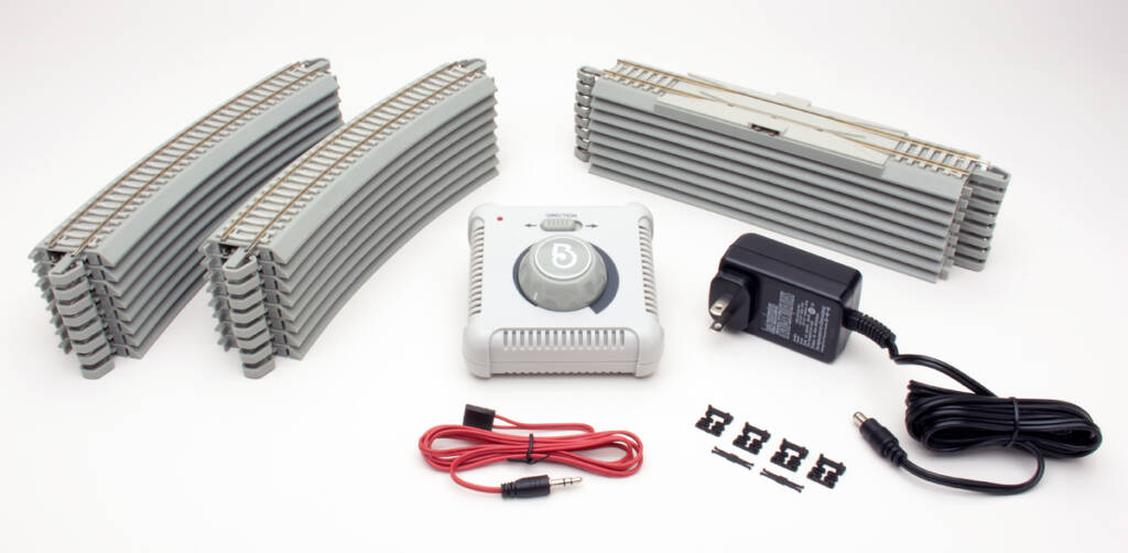 Color photo showing three stacks of HO scale track with nickel silver rail and concrete ties, power pack, speed controller, red wire, and coupler components on white background. 