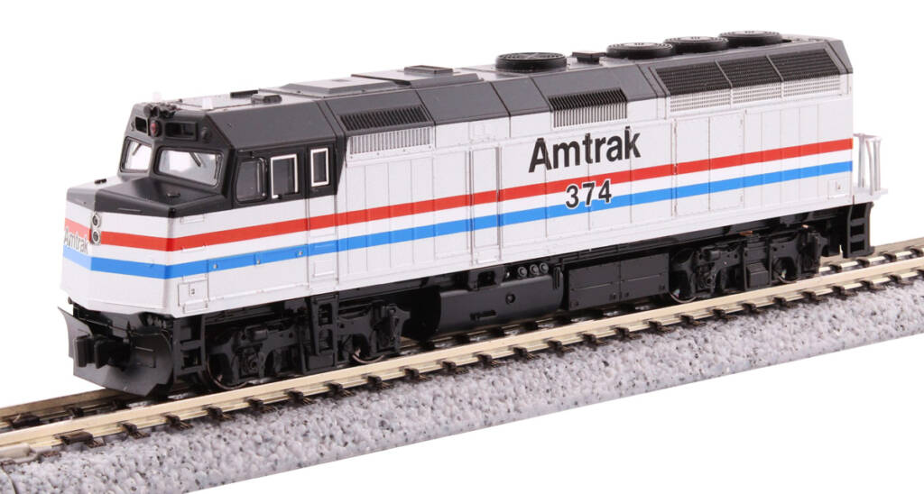 Color photo of cowl-body four-axle N scale passenger diesel painted aluminum and black with red, white, and blue stripes on piece of track with molded ballast on a white background.