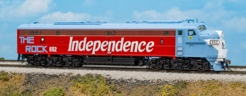 Color photo of HO scale six-axle cab unit painted red, white, and blue on scenicked base with a blue backdrop with clouds. 