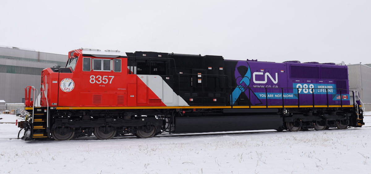 Red, white, and black locomotive with purple section of long hood and logo of 988 Lifeline