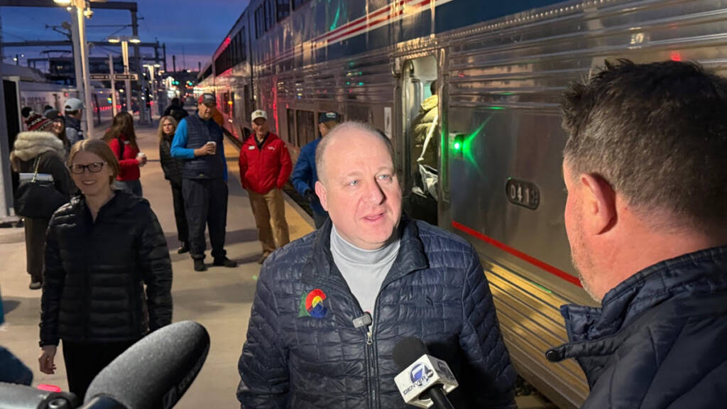 Man speaking to journalists with passenger train in background