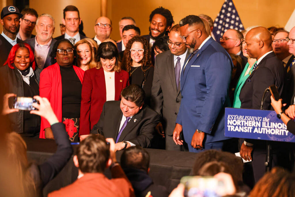 Large crowd around man signing document at table