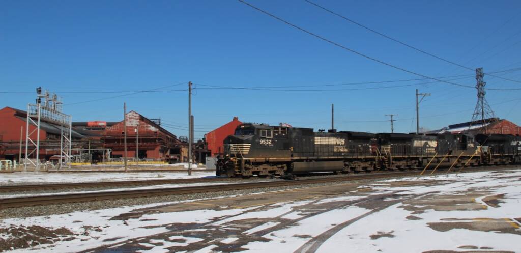 Train with black locomotives passing steel plant