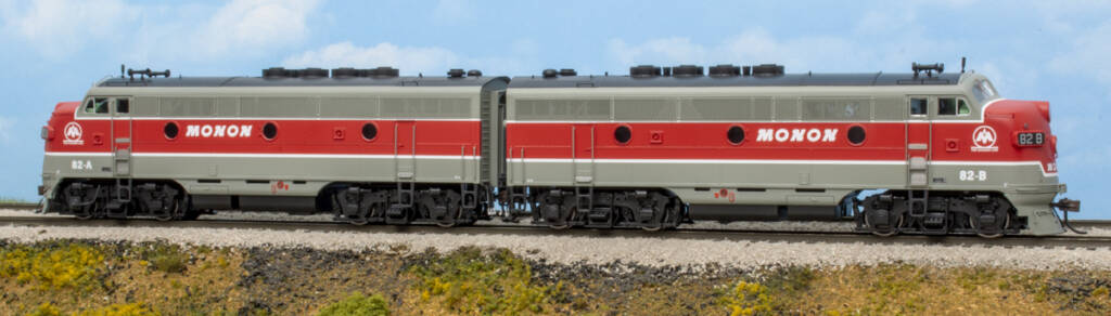 Color photo of two HO scale cab units painted red, gray, black, and white on scenicked base with a sky blue backdrop.