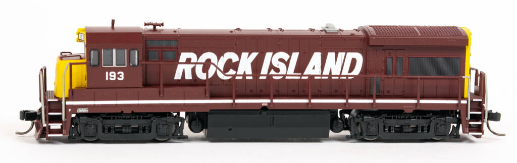 Side view of N scale diesel locomotive painted maroon, yellow, and black with red and white graphics on white background.