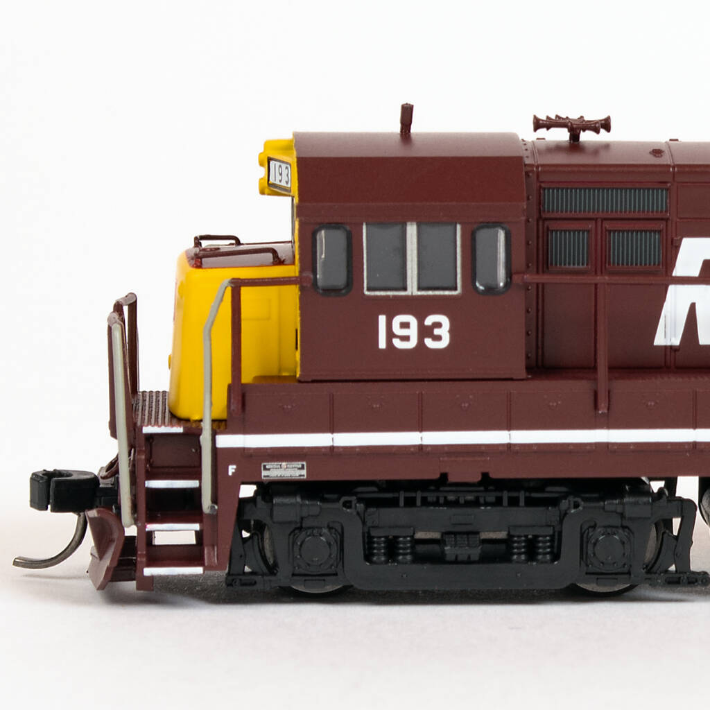 Color photo showing fireman's side of N scale diesel locomotive painted maroon and yellow with white graphics on white background.
