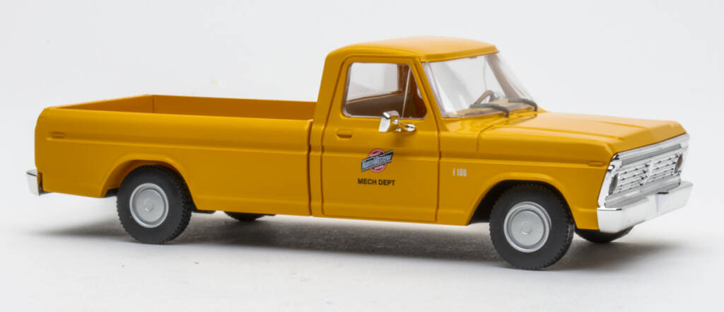 Color photo of O scale pickup truck painted yellow with red, black, and white graphics and silver wheels on white background. 