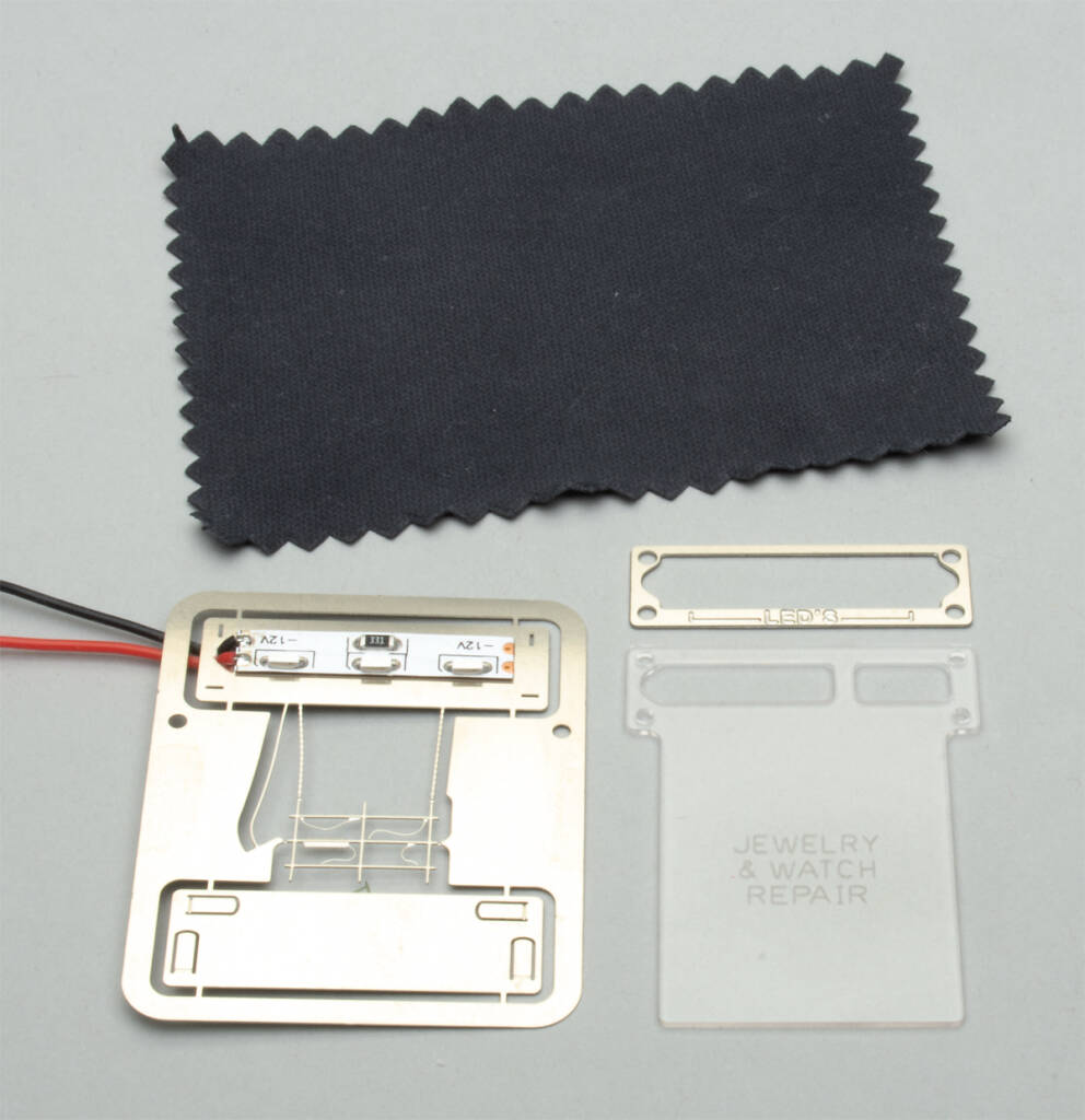 Color photo showing black cleaning cloth, etched-metal parts, red and black wires, and etched clear acrylic plastic on light gray background.