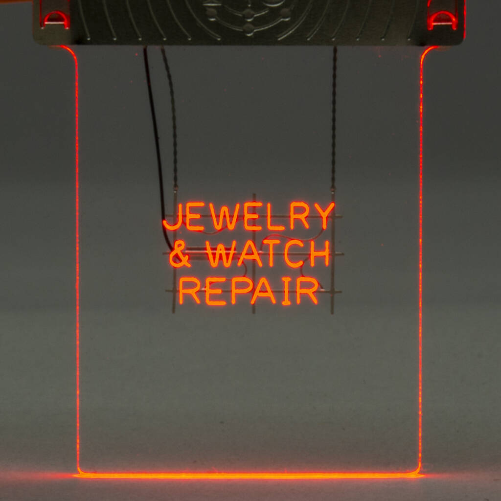 Color photo of illuminated etched-acrylic sign that reads Jewelry & Watch Repair. Metal frame is visible near the top of the frame.