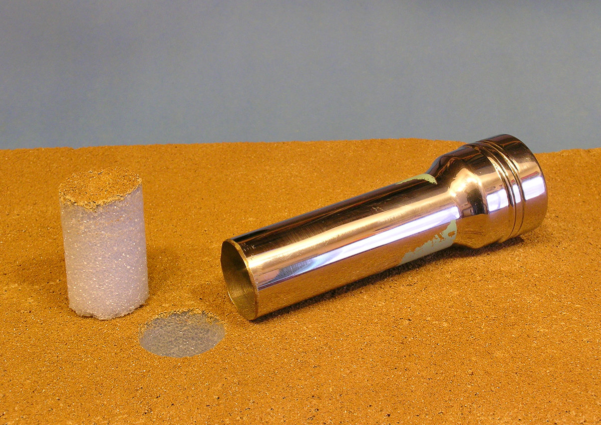 A flashlight housing sits next to a hole in a model railroad layout and the removed section of layout, which will eventually house a live cactus plants