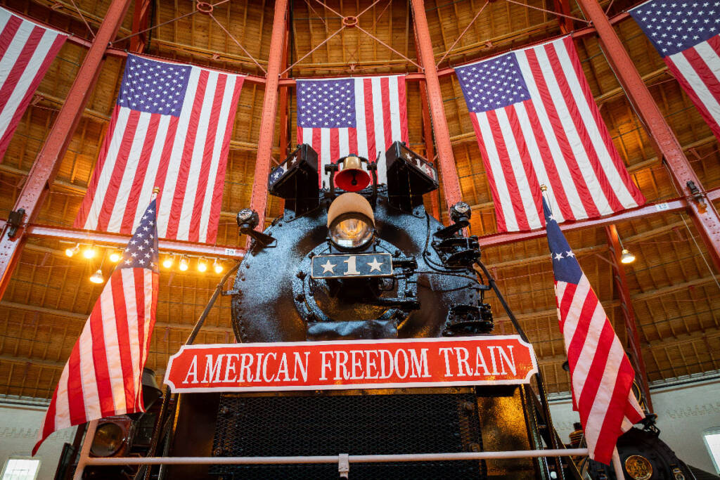 Black steam locomotive with U.S. flags in background. American Freedom Train No. 1 unveiled.