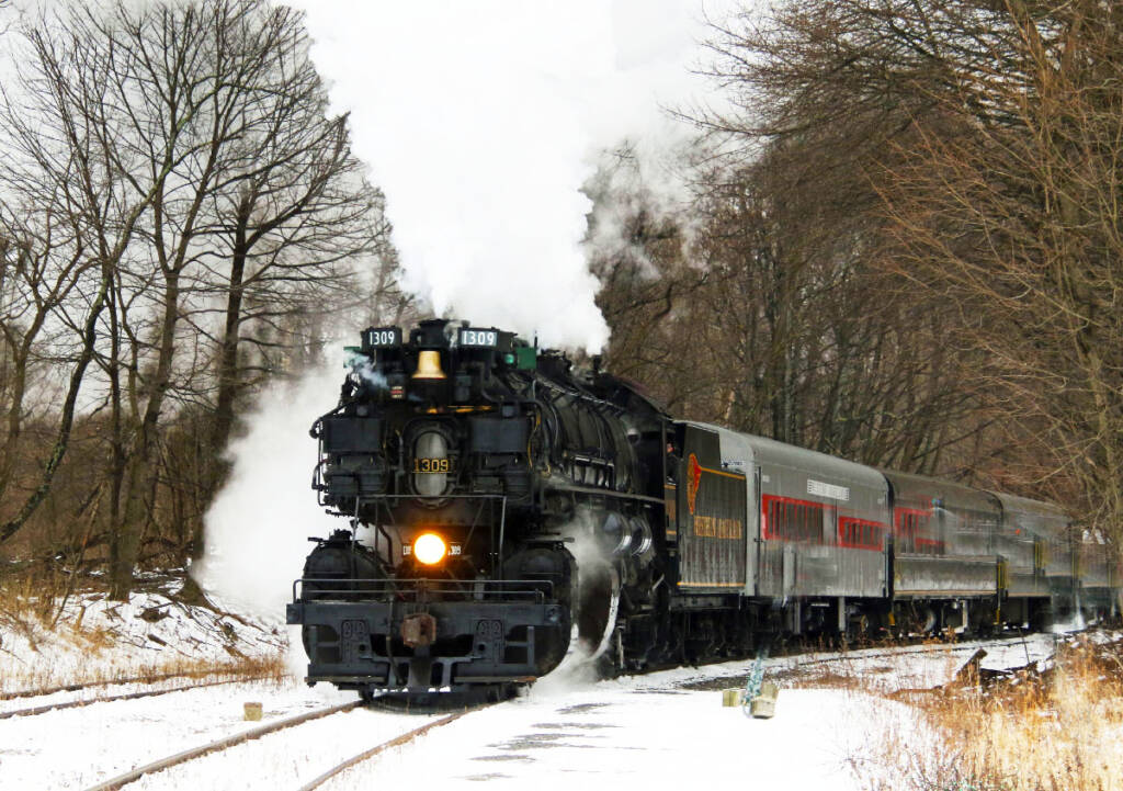 Large black steam locomotive and passenger train in a winter setting.