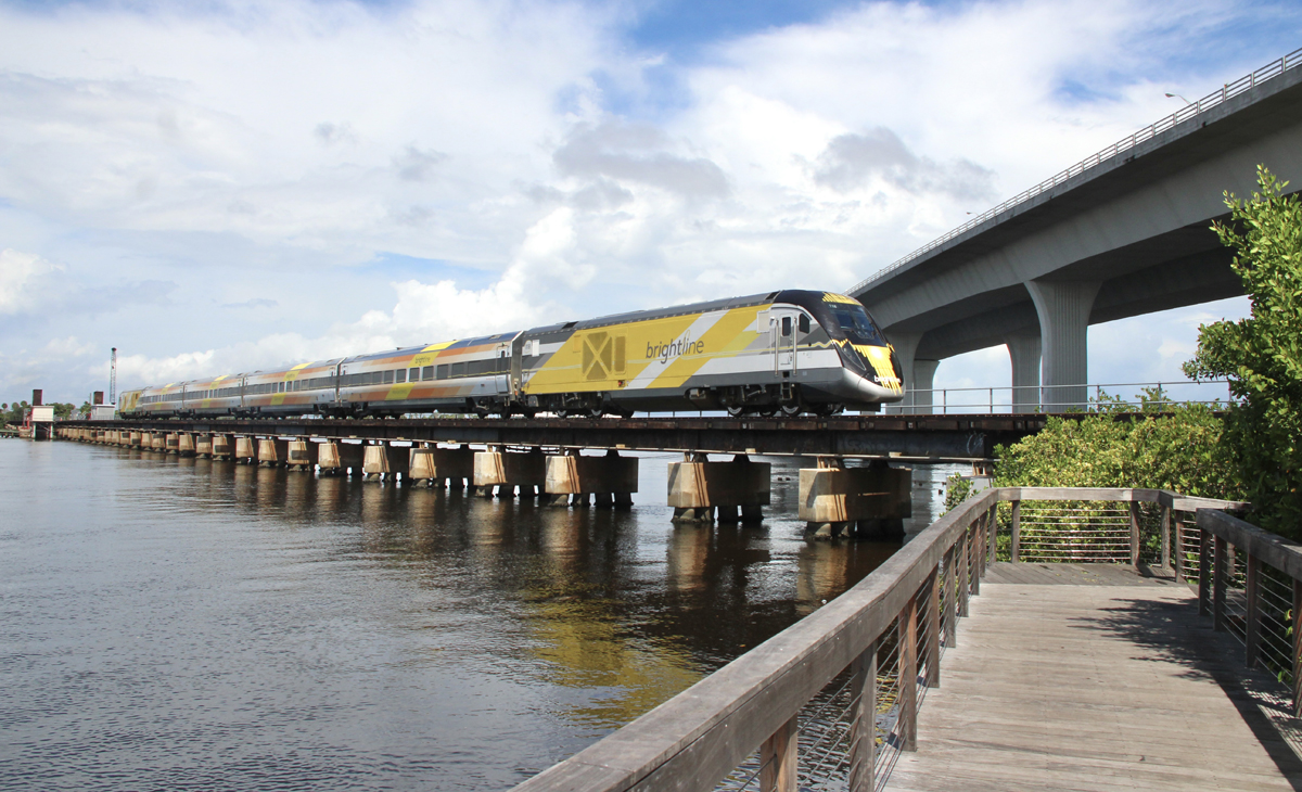 Yellow and white locomotive leads passenger train across bridge