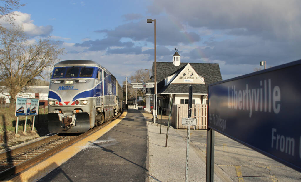 Commuter train arrives at station with station sign in foreground