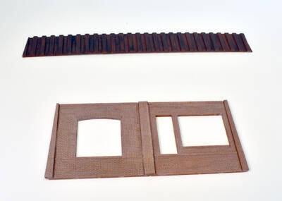 brown painted plastic model of steel retaining wall above brick wall sections on white background