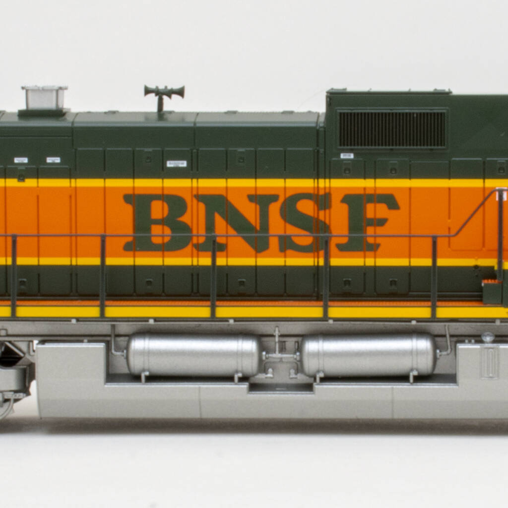 Color photo showing middle of long hood on an HO scale modern GE six-axle diesel locomotive painted orange, green, and yellow with a silver fuel tank on white background.