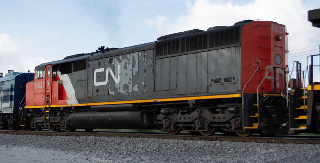 Color photo of six-axle cowl-body diesel painted red, white, and black with gray map of North America under CN “wet noodle” herald.