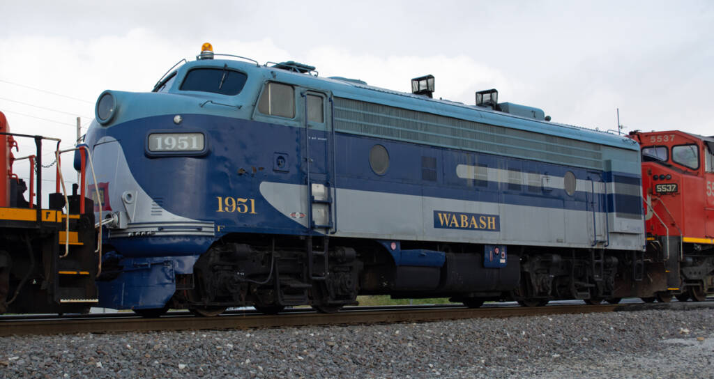 Color photo of EMD four-axle cab unit painted blue and gray with yellow graphics between two Canadian National units.