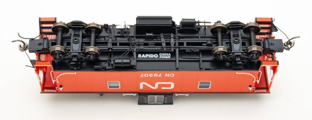 Color photo showing underbody of HO scale caboose painted red and black with white graphics on white background.