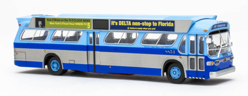 Color photo showing HO scale transit bus painted two-tone blue and silver with advertisements above the windows on white background. 