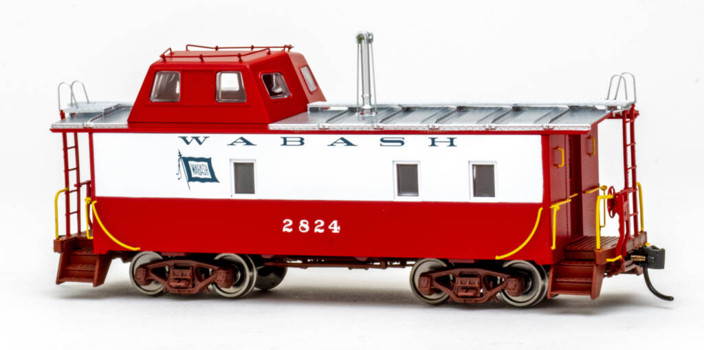 Color photo of HO scale steel caboose with streamlined offset cupola painted red and white with silver roof, oxide red trucks and end platforms, and yellow grab irons on white background. 