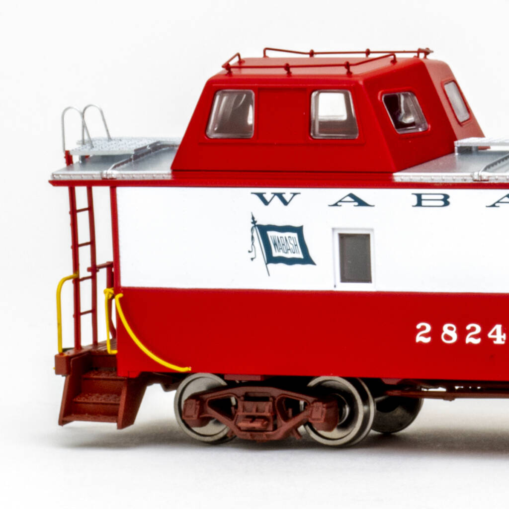 Color photo showing portion of HO scale steel caboose with streamlined offset cupola painted red and white with silver roof, oxide red trucks and end platforms, and yellow grab irons on white background.