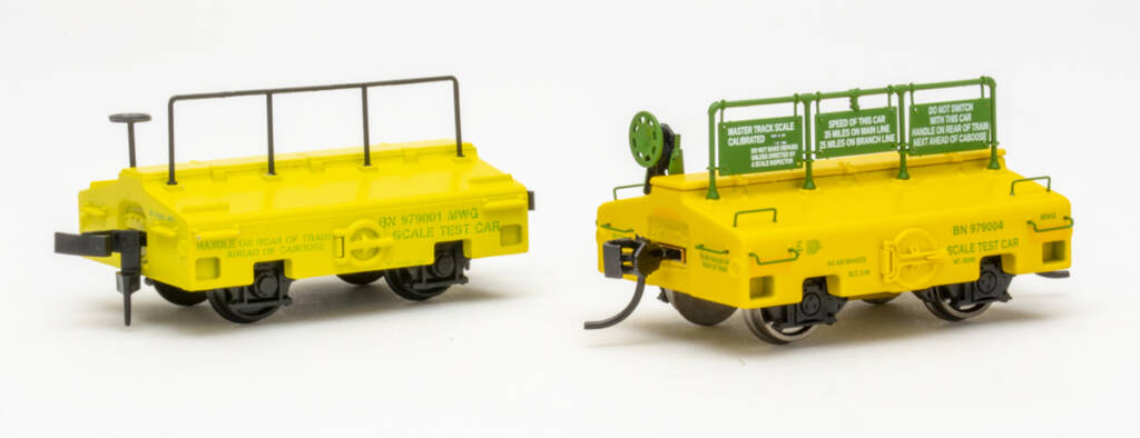 Color photo showing two HO scale test cars painted yellow with green graphics on white background.