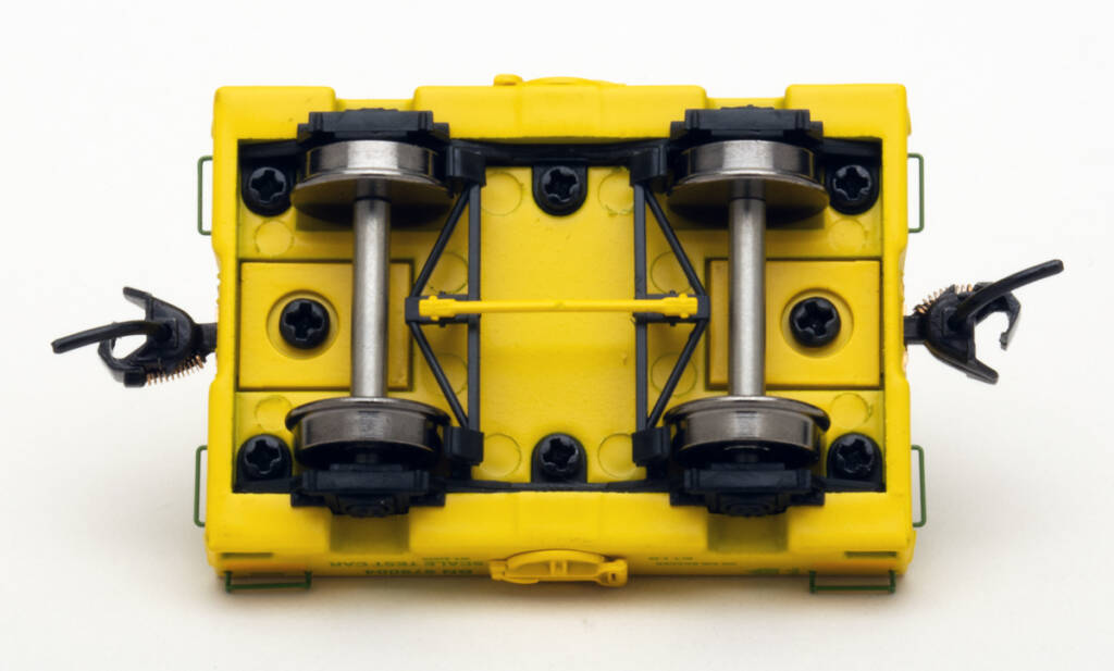 Color photo showing underbody of scale test car with yellow, black, and unpainted metal parts on white background.