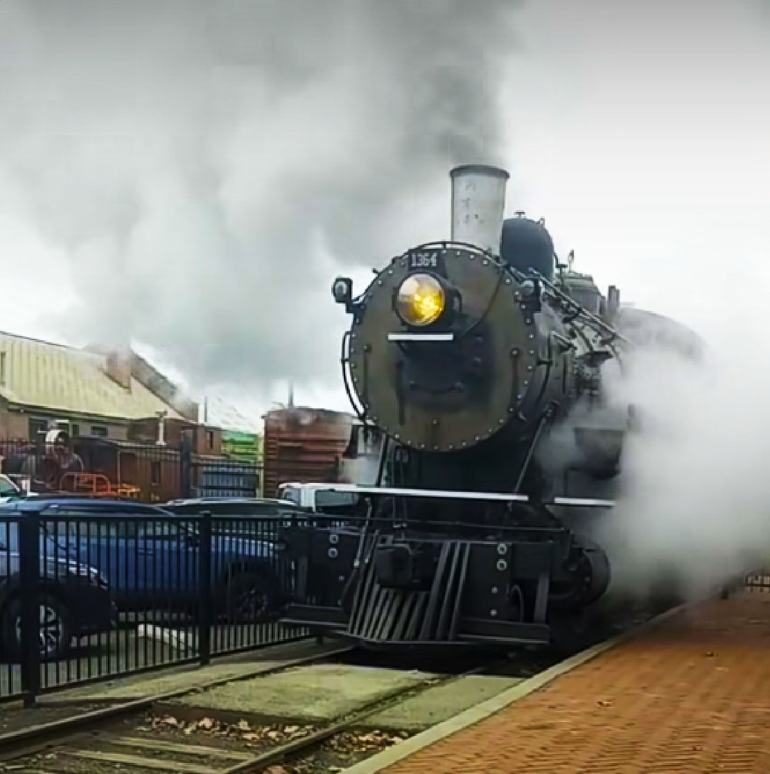 Black steam locomotive with steam and smoke along a station platform. Northern Pacific No. 1364 runs again after 73 years.