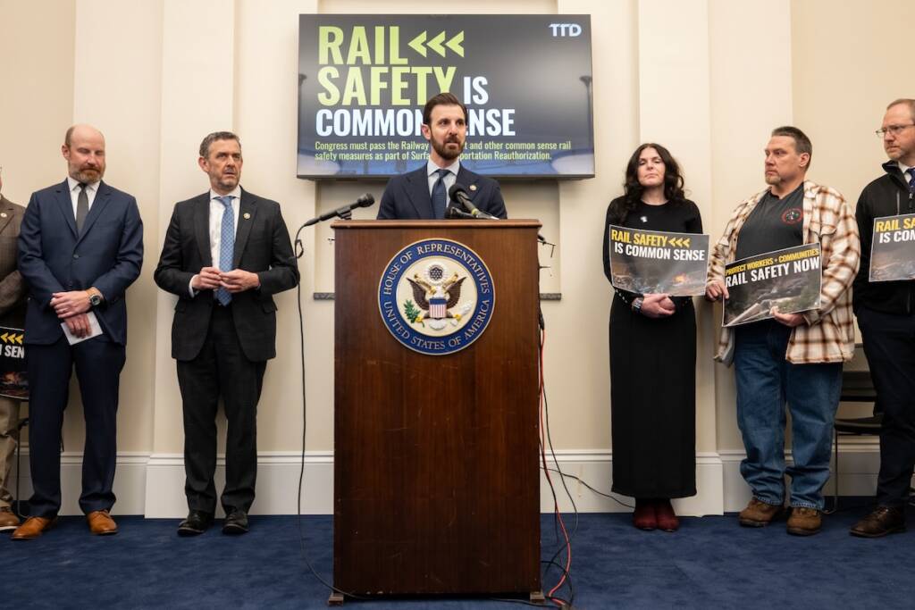 Man speaking at podium with people standing on either side