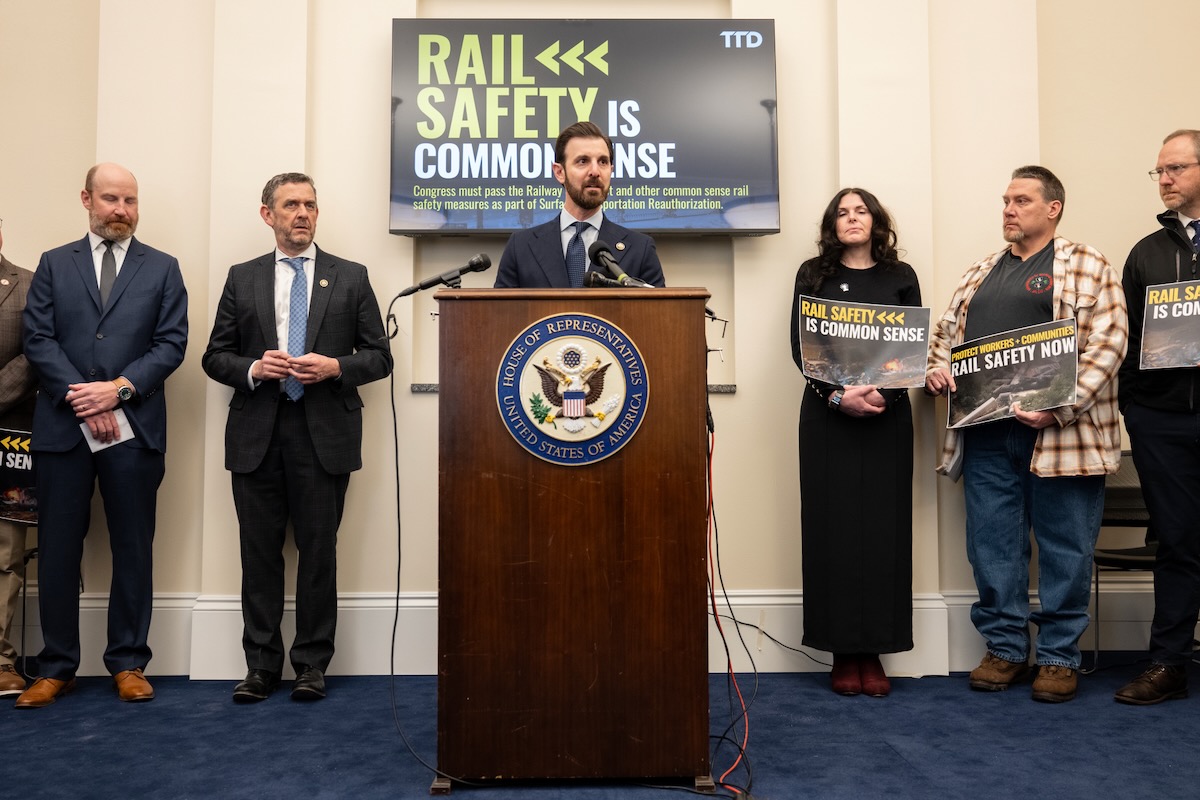 Man speaking at podium with people standing on either side