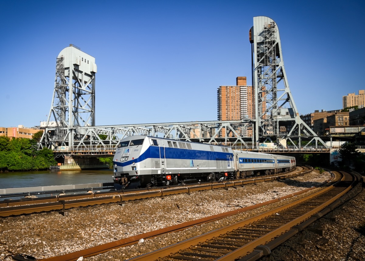 Silver and blue locomotive with commuter train passing under bridge