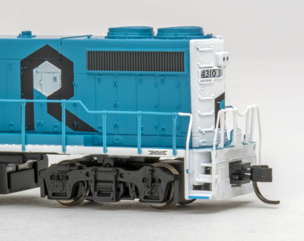 Color photo showing fireman’s side of long hood on four-axle EMD locomotive painted blue and white on white background.