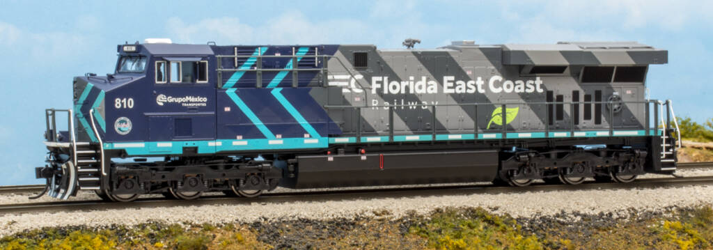 Color image of modern HO scale GE diesel locomotive painted two-tone blue, two-tone gray, and black with white and green graphics on scenicked base with a sky blue background.