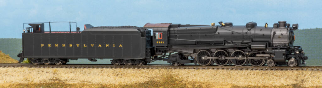 Color photo of N scale steam locomotive and tender with six-axle trucks on scenicked base with a sky blue background. 