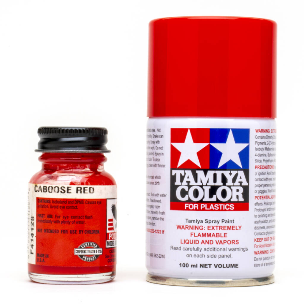 Color photo showing glass bottle of red paint with red, white, and black label and black metal lid and spray can with red, white, blue, and black graphics and red plastic cap on white background.