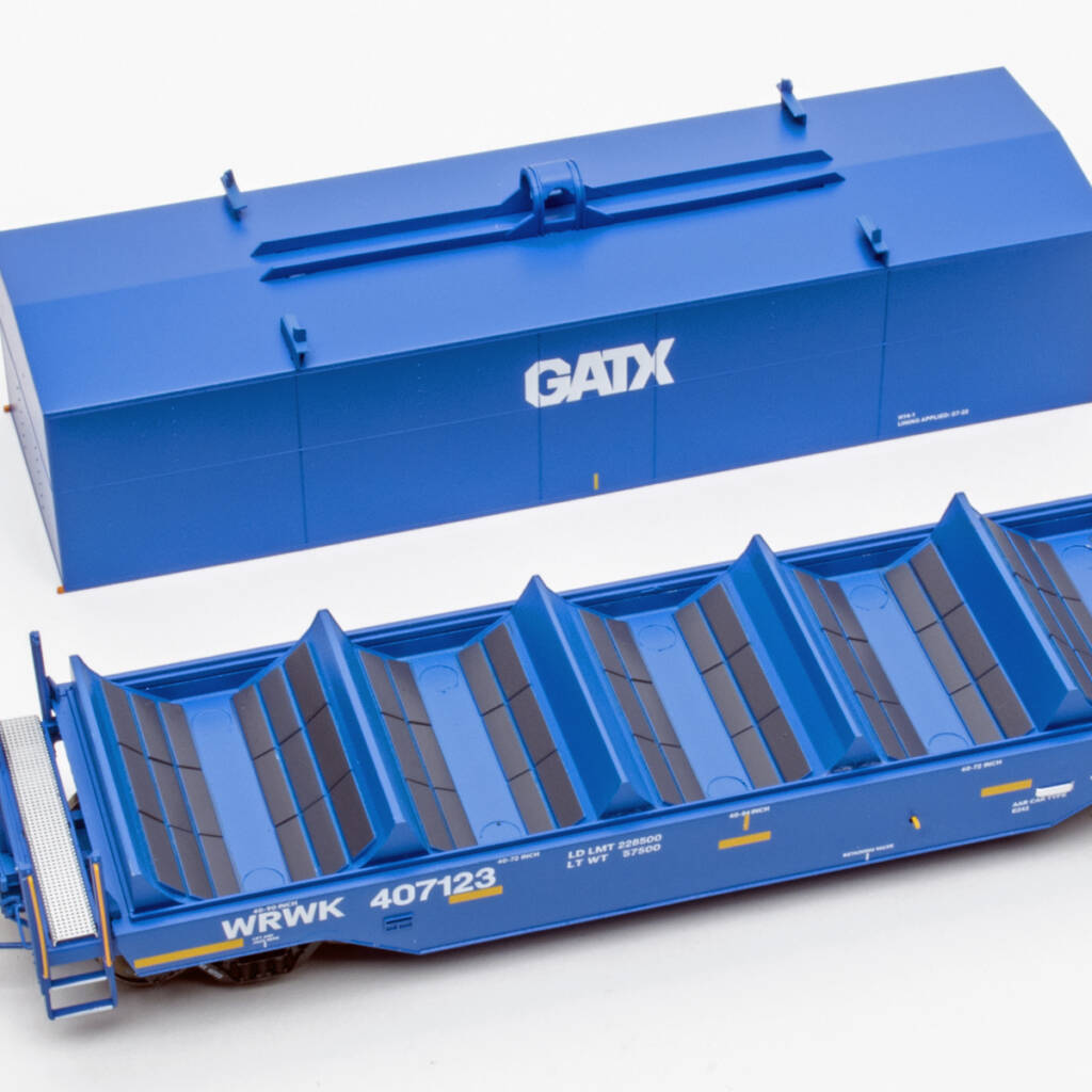 Color photo showing modern coil car with hood placed next to car on white background. The model is painted blue with yellow and white graphics and dark gray bunk liners.