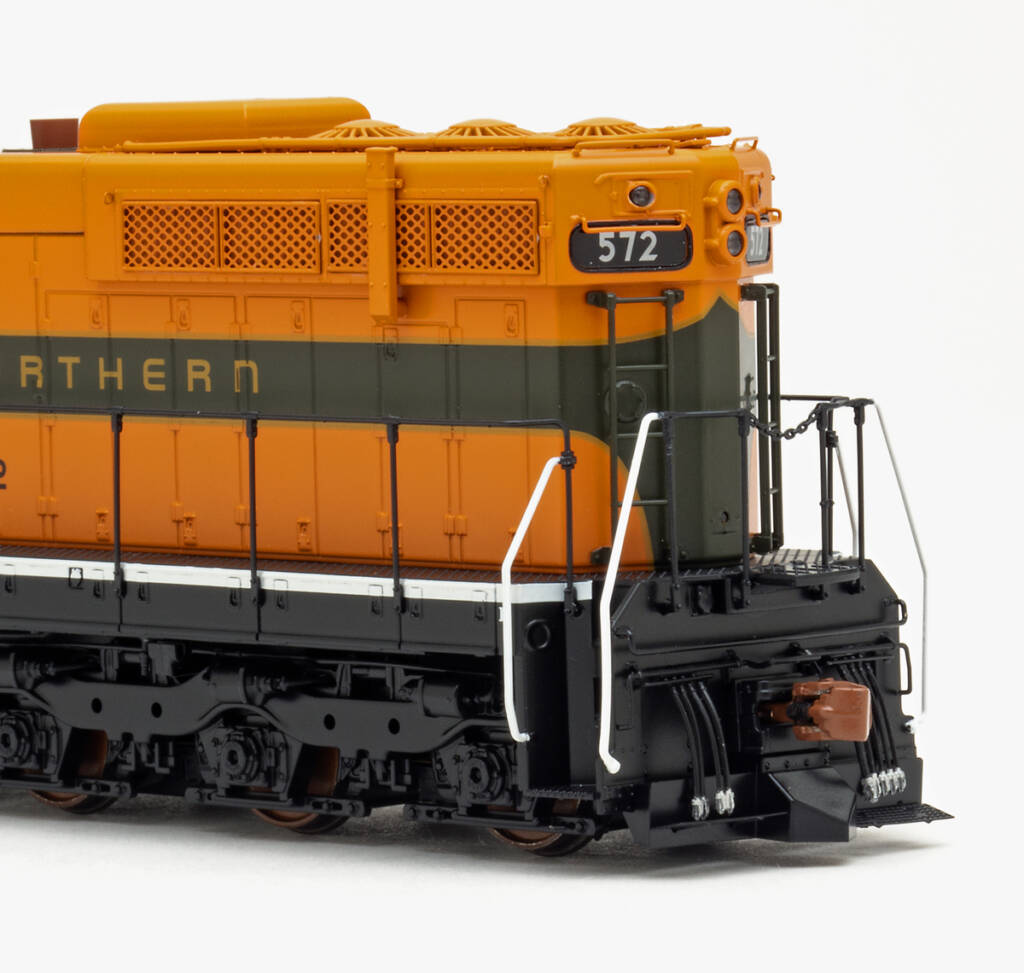 Color photo showing rear of long hood on EMD six-axle hood unit painted orange, green, and yellow with black trucks, sill, and pilot on white background.
